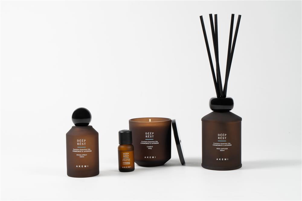 Collection of home fragrance products including a room spray, essential oil bottle, scented candle, and reed diffuser arranged on a white background.